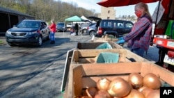 Workers from Sarver farms, right, wear protective masks, beside the onions, potatoes and vegetables they are selling to patrons driving by in their cars at the Greensburg Farmers' Market opening day, Saturday, April 25, 2020, in Greensburg, Pa.