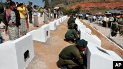 In this photo released by the Myanmar Defense Ministry, soldiers place urns containing ashes of soldiers fallen during recent fighting against ethnic Kokang rebels at a military funeral in Lashio, Myanmar, Feb. 23, 2015.