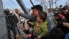 FILE - A man from Afghanistan carrying a baby cries as he pushes against the fence at the Greece-Macedonia border during a demonstration near the village of Idomeni, northern Greece, Feb. 22, 2016.