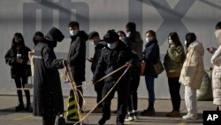 Security guards set up the barricade line as people line up to get a swab for the COVID-19 test to meet traveling requirements at a mobile coronavirus testing facility outside a commercial office buildings in Beijing, Jan. 16, 2022. 