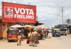 FILE - Women walk beneath an election banner for the ruling Frelimo Party in Maputo, Mozambique, Oct. 11, 2019.