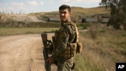 A U.S.-backed Syrian Democratic Forces fighter stands guard as trucks carrying Islamic State militants and families who surrendered in Baghuz, Syria, move to a camp, March 19, 2019. 