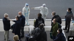 A worker in protective coverings directs members of the World Health Organization (WHO) team on their arrival at the airport in Wuhan in central China's Hubei province on Jan. 14, 2021. 