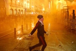 An anti-government protester prepares to throw stones at the riot police, during a protest against the new government, near the parliament square, in Beirut, Lebanon, Jan. 22, 2020.