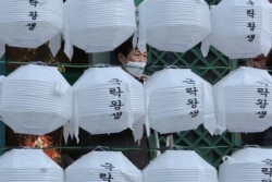 A woman wearing a face mask stands behind lanterns decorated for upcoming celebration of Buddha's birthday on April 30, at Jogye temple in Seoul, South Korea, Tuesday, Feb. 18, 2020.
