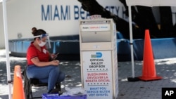 FILE - A poll worker monitors a ballot drop box for mail-in ballots outside a polling station during early voting, Aug. 7, 2020, in Miami Beach, Fla.