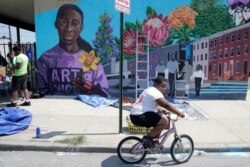 A boy rides his bicycle, July 29. 2019, after volunteering to paint a mural outside the New Song Community Church in the Sandtown section of Baltimore.