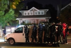Portland police hang off the side of a riot van while searching for protesters in the Laurelhurst neighborhood after dispersing a crowd of about 200 people from in front of the Multnomah County Sheriff's Office on Aug. 8, 2020, in Portland, Ore.