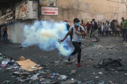 An anti-government protester prepares to throw back a tear gas canister fired by police during clashes between Iraqi security forces and demonstrators, in downtown Baghdad, Iraq, Nov. 13, 2019.