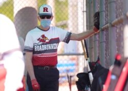 FILE - John Journey, 86, wearing a mask to the prevent the spread of COVID-19, listens to his team coach speak in the dugout before a 65-and-over league softball game, April 20, 2021, in Richardson, Texas.