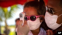 A little girl wearing a face mask amid the new coronavirus pandemic gets her temperature taken at a police checkpoint, at the entrance to the province of Havana, Cuba, Monday, Aug. 10, 2020