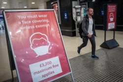 A man, not wearing a face covering, passes signs telling travelers they must wear face masks unless they are exempt, as he leaves Victoria station during the evening rush hour, in central London, Sept. 23, 2020.