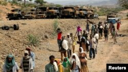 FILE - Villagers return from a market to Yechila town in south central Tigray walking past scores of burned vehicles, in Tigray, Ethiopia, July 10, 2021. 