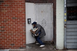 Francisco Rami­rez peers through a hole in a fence while looking for an address to deliver a box of groceries to a man in need Saturday, April 18, 2020, in the Queens borough of New York.