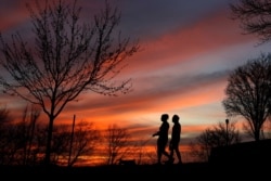 A couple walk a dog at sunset March 25, 2020, in Kansas City, Mo. The city, along with neighboring counties, is under Stay at Home orders to help prevent the spread of COVID-19, the disease caused by the new coronavirus.