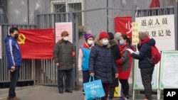 FILE - Residents wait to enter a checkpoint with a sign which reads "Returnees to Beijing registration point" in Beijing, Feb. 13, 2020. 