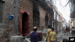 FILE - Residents look at a house of a family belonging to the Ahmadi sect, which was torched by angry mob in Gujranwala, Pakistan, July 28, 2014.