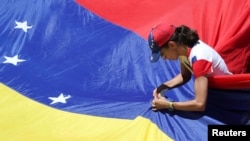 Una partidaria del líder opositor venezolano, Juan Guaidó, fija una bandera durante un mitin contra el gobierno del presidente venezolano Nicolás Maduro en Caracas. Abril 6, 2019.