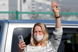A woman waves from outside Daikoku Pier Cruise Terminal as she communicates via phone with a passenger on the cruise ship Diamond Princess, as the vessel's passengers continue to be tested for coronavirus, in Yokohama, Japan, Feb. 13, 2020.