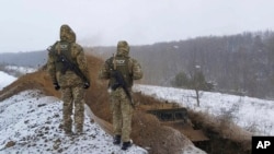 FILE - In this image provided by the Ukrainian Board Guard Press Office, Ukrainian border guards watch as a special vehicle digs a trench on the Ukraine-Russia border close to Sumy, Ukraine, Dec. 21, 2021. 