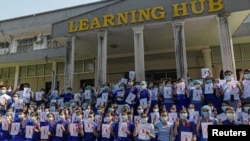 Teachers from Yangon University of Education wear red ribbons and pose with a three-finger salute as they take part in demonstration against the military coup in Yangon, Myanmar, February 5, 2021. REUTERS/Stringer