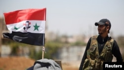 A Syrian army soldier stands next to a Syrian flag in Umm al-Mayazen, in the countryside of Daraa, Syria, July 10, 2018. 