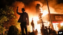 Protestors demonstrate outside of a burning fast food restaurant, May 29, 2020, in Minneapolis. Protests over the death of George Floyd, a black man who died in police custody Monday, broke out in Minneapolis for a third straight night.