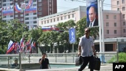 Місцеві мешканці Північної Кореї проходять повз портрета президента Росії Путіна біля прапорів Північної Кореї та Росії в Пхеньяні 20 червня 2024 року, виставлених з нагоди візиту Путіна. Фото: Kim Won Jin/AFP