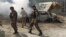 FILE - Afghan security forces walk past a burning car after a group of Taliban insurgents stormed a compound used by Afghanistan's intelligence agency in Kabul, Afghanistan, July 7, 2015.