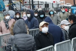 Patients wear personal protective equipment while maintaining social distancing as they wait in line for a COVID-19 test at Elmhurst Hospital Center, March 25, 2020, in New York.