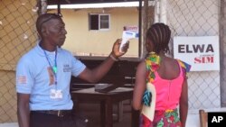 FILE - A unidentified family member (R) of a 10-year-old boy who contracted Ebola, has her temperature taken by a health worker at an Ebola clinic on the outskirts of Monrovia, Liberia, Nov. 20, 2015. 