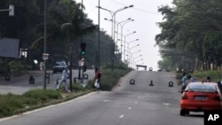 People walk on a road blocked by armed forces near the Ivorian state television station in the Cocody district of Abidjan, 18 Dec 2010