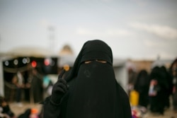 FILE - A woman poses at Al-Hol camp, March 31, 2019, which holds families of Islamic State members, near Hasakeh, Syria.