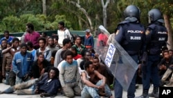 FILE - Migrants sit on the ground next to Spanish police officers after storming a fence to enter the Spanish enclave of Ceuta, Spain, Feb. 17, 2017.