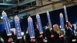 Volunteers hold up signs as they wait for Democratic presidential candidates to enter the media spin room near the end of a Democratic presidential primary debate, Feb. 7, 2020, at Saint Anselm College in Manchester, N.H.
