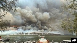 Boats are pulled ashore as smoke and wildfires rage behind Lake Conjola, Australia, Jan. 2, 2020.