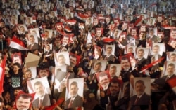 FILE - Members of the Muslim Brotherhood and supporters of Egypt's President Mohamed Mursi hold pictures of him as they react after the Egyptian army's statement was read out on state TV, at the Raba El-Adwyia mosque square in Cairo, July 3, 2013.