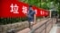 A man wearing a face mask to protect against the spread of the new coronavirus walks past a propaganda banner encouraging people to sort their garbage in Beijing, June 24, 2020.