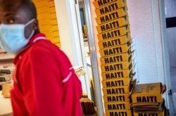 In this March 14, 2020 file photo, boxes of rum are stacked as a duty free employee wears a mask amid the COVID-19 pandemic while working at Toussaint Louverture International Airport in Port-au-Prince, Haiti.