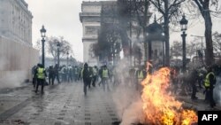 Protesters wearing yellow vests stand next to a burning tree as they demonstrate against the rising costs of living that they blame on high taxes near the Arc de Triomphe on the Champs-Elysees avenue in Paris, Dec. 8, 2018.