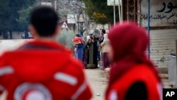 FILE - Members of the Syrian Red Cross stand near aid vehicles loaded with food and other supplies that entered the besieged town of Madaya about 15 miles (24 kilometers) northwest of Damascus, Syria, Jan. 11, 2016.