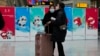 Passengers wearing masks to protect them from the coronavirus stand near Beijing Winter Olympics posters at the South Train Station in Beijing, Jan. 14, 2022.