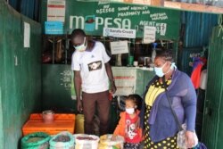 Jane Mutuku, 49, a Mukuru Kayaba resident, buys food using Sarafu, an e-voucher community currency. Sarafu has been a lifesaver for her and her six children; work has been hard to come by for her because of the COVID-19 pandemic. (Mohammed Yusuf/VOA)