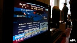Relatives of the passengers on board the Malaysia Airlines Flight 370 that went missing on March 8, 2014 stand near a TV showing a live broadcast of the missing AirAsia Flight 8501 from Surabaya to Singapore, during their year-end gathering at a house in 