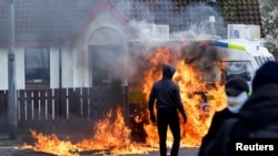 Dissident republicans stand near a burning police car after an anti-Good Friday Agreement rally on the 25th anniversary of the peace deal, in Londonderry, Northern Ireland, April 10, 2023.