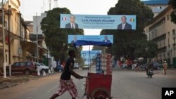 Seorang pedagang kaki lima di Guinea melawati sebuah spanduk di jalan yang memperlihatkan gambar Presiden Perancis Hollande dan Presiden Guinea Alpha Conde di Conakry, Guinea (26/11/2014). 