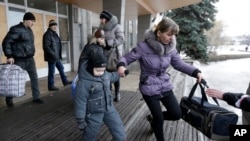 People carry their belongings as they walk to a bus to leave the town of Debaltseve, Ukraine, Saturday, Jan. 31, 2015.