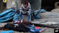 This photo provided by the Syrian Civil Defense White Helmets, which has been authenticated based on its contents and other AP reporting, shows a Syrian boy sitting next to bodies after artillery fire struck the Jub al-Quba district in Aleppo, Syria, Nov.