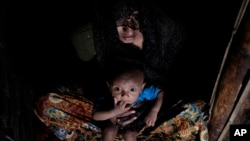 Mohsena Begum, a Rohingya who escaped to Bangladesh from Myanmar, holds her child and sits at the entrance of a room of an unregistered refugee camp in Teknaf, near Cox's Bazar, a southern coastal district south of Dhaka, Bangladesh, Dec. 2, 2016.