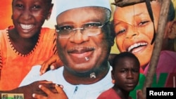A boy sits in front of an electoral campaign poster for Malian presidential candidate Ibrahim Boubacar Keita, in Timbuktu, Mali, July 25, 2013.